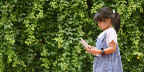 Cute girl in casual clothes listening to music and learning on your digital tablet in the park.