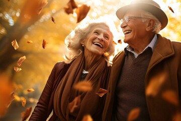 a smiling elderly couple, backlit by the gentle afternoon sun, merrily throwing handfuls of crisp autumn leaves, with blurred motion effect - obrazy, fototapety, plakaty