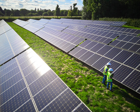 Aerial Drone Shot Of Engineers Inspecting Solar Panels In Field Generating Renewable Energy