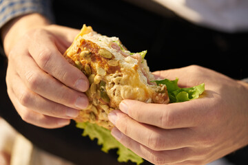 Men's hands hold a fresh sandwich, a clear and sunny day.