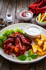 Buffalo wings with ranch dressing and French fries on wooden table
