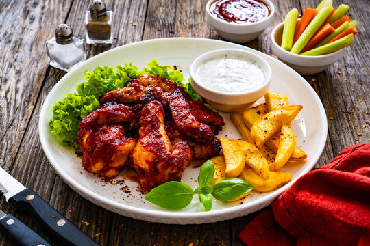 Buffalo wings with ranch dressing and French fries on wooden table
