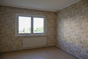 Unrenovated empty room with an old patterned wallpaper on the walls, concept for housing and...