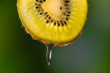 Macro photography. Close-up of a slice of kiwi with splashes, drops of water or juice on a blurry green background. Fruit background - obrazy, fototapety, plakaty