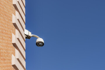 A surveillance camera placed in a corner of a building on a day with the sky completely free of...