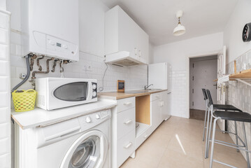 Kitchen furnished on one of the walls with white furniture, integrated appliances, a gas boiler and light wood-colored countertop