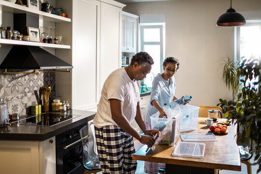 Senior African American couple recycling plastic waste in their kitchen at home