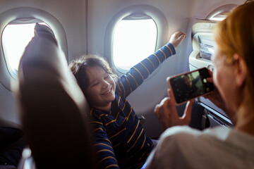 Happy young boy posing for a picture taken by his mother while travelling and flying together on a plane