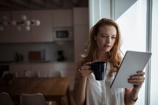 Young woman using her tablet in the living room at home - Powered by Adobe