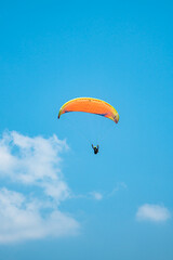 An adrenaline-pumping extreme sport, paragliding against the clear blue sky. Paraglider flying with his parachute above the sky with a background of blue sky and white clouds in a sunny day.