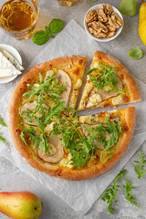 Delicious pizza with pears, gorgonzola cheese, walnuts and arugula on a gray concrete background.