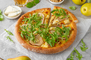 Delicious pizza with pears, gorgonzola cheese, walnuts and arugula on a gray concrete background.