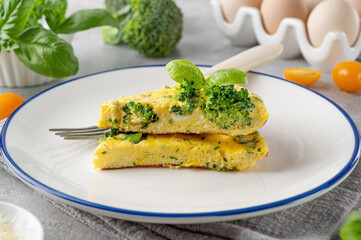 Omelette with broccoli, cheese and fresh basil on a plate on a gray concrete background. Healthy breakfast.