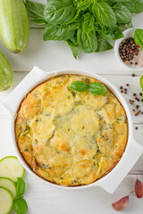 Zucchini casserole in cream cheese sauce in a white baking dish on a white wooden background. Healthy comfort vegetarian food