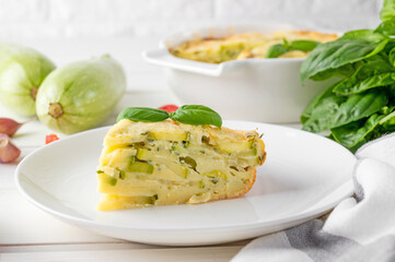 Zucchini casserole in cream cheese sauce in a white baking dish on a white wooden background. Healthy comfort vegetarian food