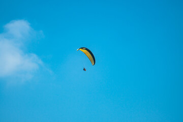 An adrenaline-pumping extreme sport, paragliding against the clear blue sky. Paraglider flying with his parachute above the sky with a background of blue sky and white clouds in a sunny day.