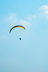 An adrenaline-pumping extreme sport, paragliding against the clear blue sky. Paraglider flying with his parachute above the sky with a background of blue sky and white clouds in a sunny day.