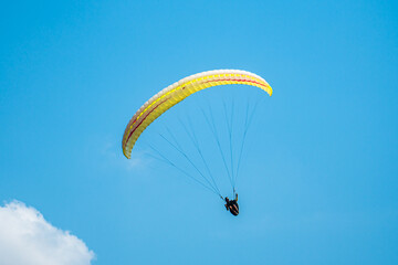An adrenaline-pumping extreme sport, paragliding against the clear blue sky. Paraglider flying with his parachute above the sky with a background of blue sky and white clouds in a sunny day.