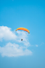 An adrenaline-pumping extreme sport, paragliding against the clear blue sky. Paraglider flying with his parachute above the sky with a background of blue sky and white clouds in a sunny day.