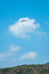 Paragliding attraction flying across hilly areas and clear blue skies. Paragliding is a sport that stimulates adrenaline by flying using a parachute in the wide sky