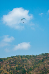 Paragliding attraction flying across hilly areas and clear blue skies. Paragliding is a sport that stimulates adrenaline by flying using a parachute in the wide sky