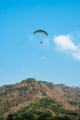 Fototapeta na wymiar Paragliding attraction flying across hilly areas and clear blue skies. Paragliding is a sport that stimulates adrenaline by flying using a parachute in the wide sky
