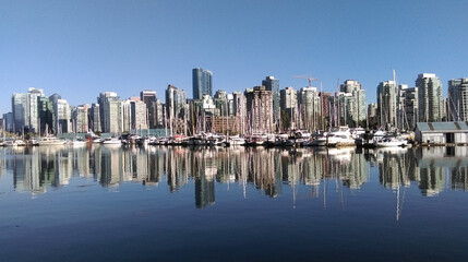 On a sunny day, a row of skyscrapers is reflected in the water (Vancouver, Canada)