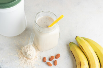 Glass jar of protein milkshake drink or smoothie and whey protein powder in measuring spoon, bananas, almond nuts on a white background. sport nutrition, bodybuilding food supplements