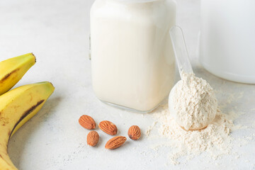 Whey protein powder in measuring spoon, glass jar of protein milkshake drink or smoothie, bananas and almond nuts on a white background. sport nutrition, bodybuilding food supplements
