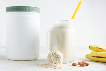 Whey protein powder in measuring spoon, glass jar of protein milkshake drink or smoothie, bananas and almond nuts on a white background. sport nutrition, bodybuilding food supplements