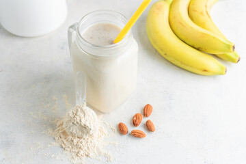 Glass jar of protein milkshake drink or smoothie and whey protein powder in measuring spoon, bananas, almond nuts on a white background. sport nutrition, bodybuilding food supplements