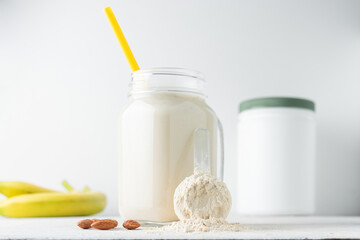 Whey protein powder in measuring spoon, glass jar of protein milkshake drink or smoothie, bananas and almond nuts on a white background. sport nutrition, bodybuilding food supplements