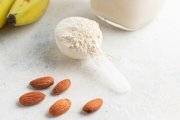 Whey protein powder in measuring spoon, glass jar of protein milkshake drink or smoothie, bananas and almond nuts on a white background. sport nutrition, bodybuilding food supplements