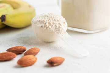 Whey protein powder in measuring spoon, glass jar of protein milkshake drink or smoothie, bananas and almond nuts on a white background. sport nutrition, bodybuilding food supplements