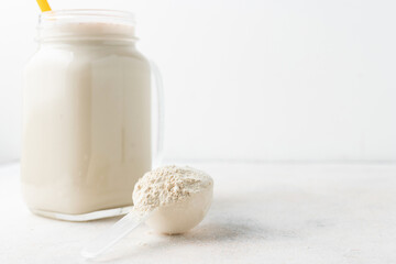 Whey protein powder in measuring spoon and glass jar of protein milkshake drink or smoothie on a white background. sport nutrition, bodybuilding food supplements