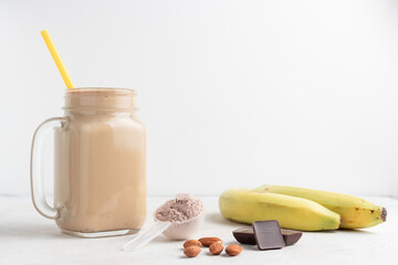 Glass jar of protein milkshake drink or smoothie and whey protein powder in measuring spoon,...