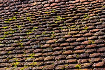 Weathered beaver tail roof tiles in different red clay colors on the old roof of an historic...