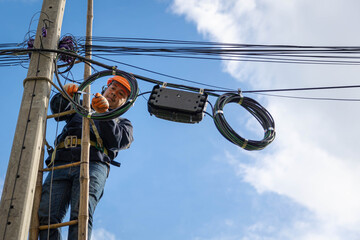 A technician working on ladder carefully for maintenance fiber optic wires attached to electric poles. Safety equipment and Operational safety. - obrazy, fototapety, plakaty