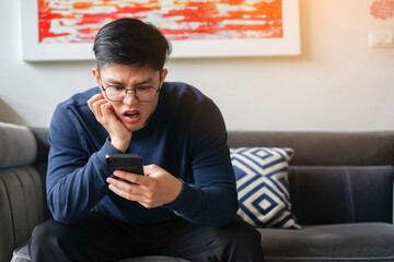 close up young asian man frowned on face with shock feeling while using smartphone to reading about fake news and rumor in home for people lifestyle concept - obrazy, fototapety, plakaty
