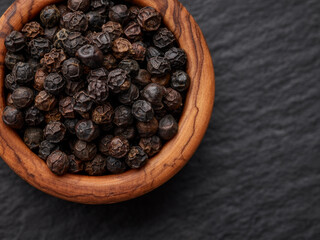 Black pepper in wooden bowl over black stone surface
