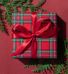 Christmas concept composition with tartan pattern gift box on the red background. Winter holiday greeting card.