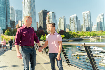 Middle aged positive gay couple, two homosexual men holding hands looking at each other walking