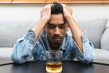 melancholy young Asian man drinks alcoholic whisky alone at home feeling dizzy after drunk