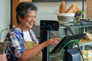 Asian retired woman gray hair, cafe owner, businessman, small business coffee shop Standing cash register counter check out customers' money smiling beautifully next bakery cabinet. family business