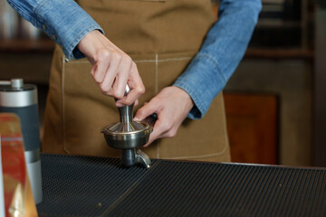 Young Asian business barista in a dark blue shirt wearing a brown apron. Grind coffee beans and brew coffee behind the coffee machine counter in a coffee shop. small family business
