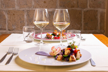 Insalata di polpo con patate viola e pomodori servita come antipasto in un ristorante elegante con un calice di vino bianco