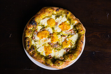Pizza napoletana gourmet con pesto di basilico, pomodori gialli, mozzarella e pancetta servita in una pizzeria napoletana 