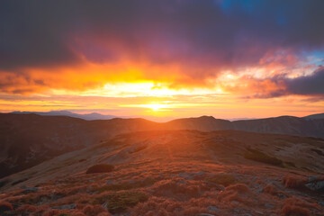 Naklejka premium Bright orange sunset on Carpathian mountain top hill. Colorful clouds sky and highland range in background. Autumn scene. Beautiful nature summer landscape. Travel, tourism, holiday, trekking, hiking