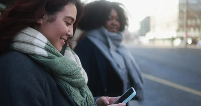 Multiracial women waiting at bus station with city in background - Asian girl using mobile phone outdoor 