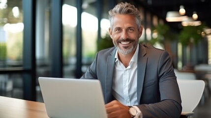Smiling mature businessman in eyeglasses working on laptop in office